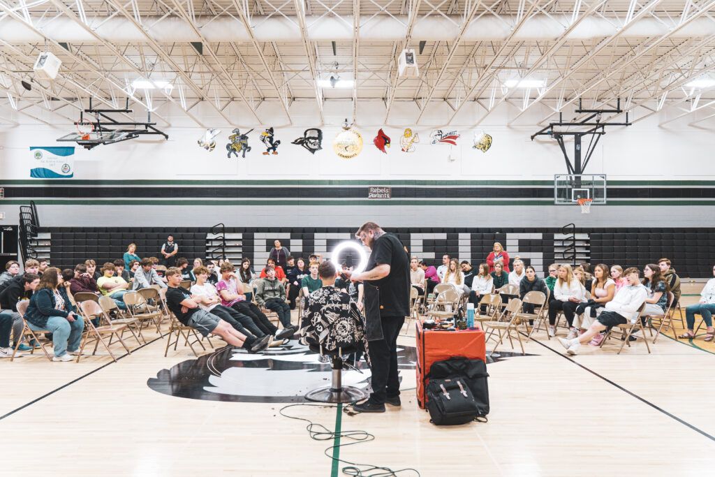 Josh Cutting a students hair in front of the student body while giving a presentation